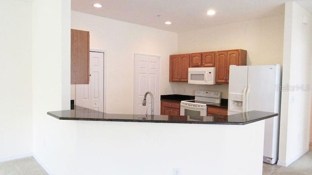 kitchen featuring sink, white appliances, kitchen peninsula, and dark stone counters