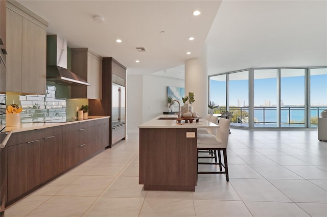 kitchen featuring wall chimney range hood, a breakfast bar, sink, and light tile patterned flooring