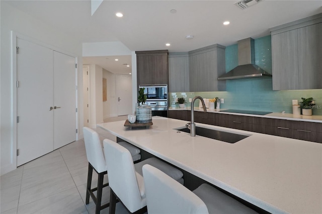 kitchen with decorative backsplash, sink, wall chimney range hood, light tile patterned floors, and a kitchen breakfast bar