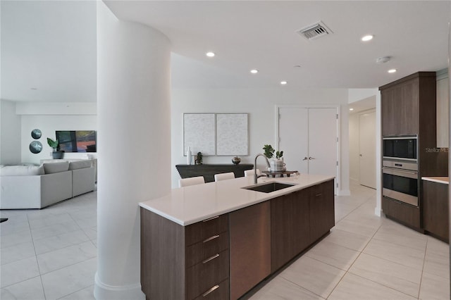 kitchen with sink, dark brown cabinetry, oven, and light tile patterned floors