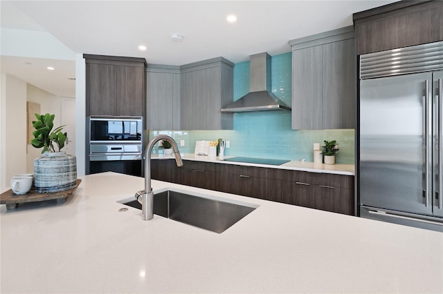 kitchen with decorative backsplash, stainless steel appliances, wall chimney range hood, and sink