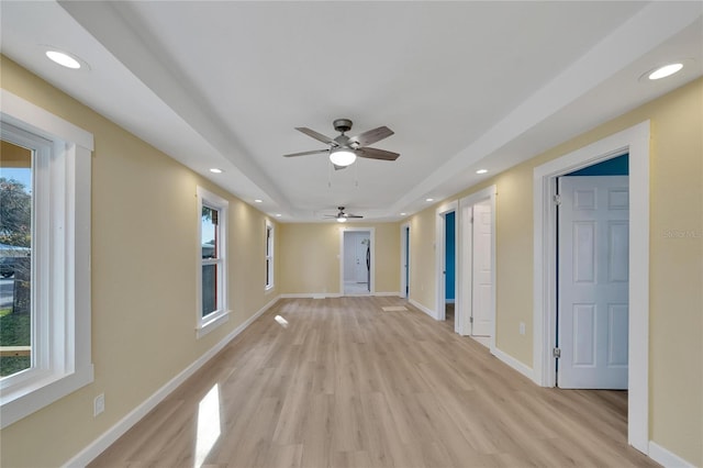 empty room with a raised ceiling, ceiling fan, and light hardwood / wood-style flooring