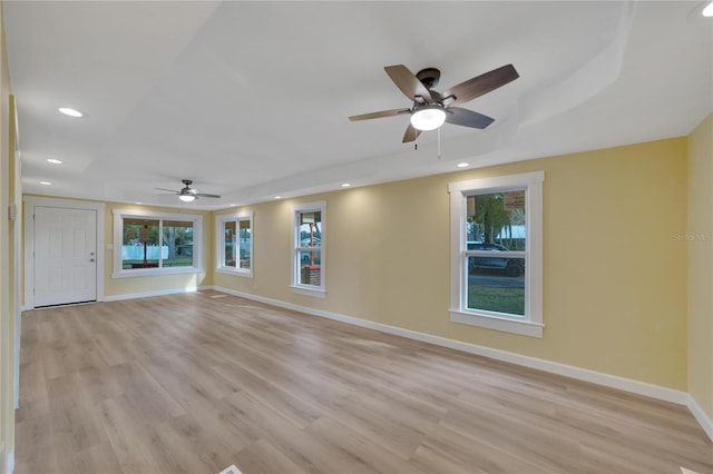 spare room with a tray ceiling, ceiling fan, and light wood-type flooring