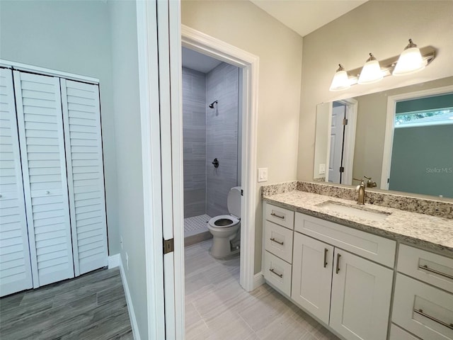 bathroom with tile flooring, toilet, large vanity, and tiled shower