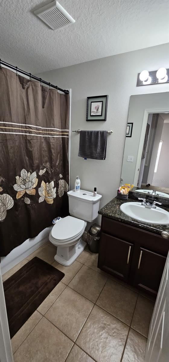 bathroom featuring tile floors, a textured ceiling, vanity, and toilet