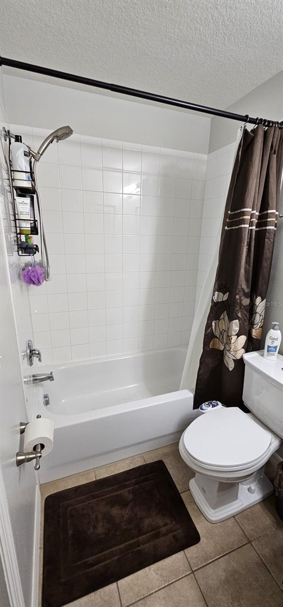 bathroom featuring shower / bathtub combination with curtain, a textured ceiling, toilet, and tile floors