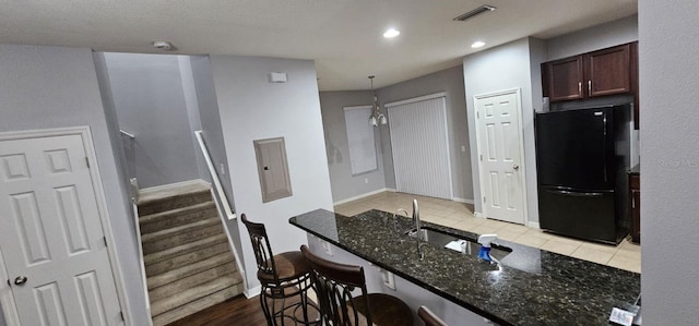 kitchen featuring wood-type flooring, dark stone countertops, black refrigerator, hanging light fixtures, and sink