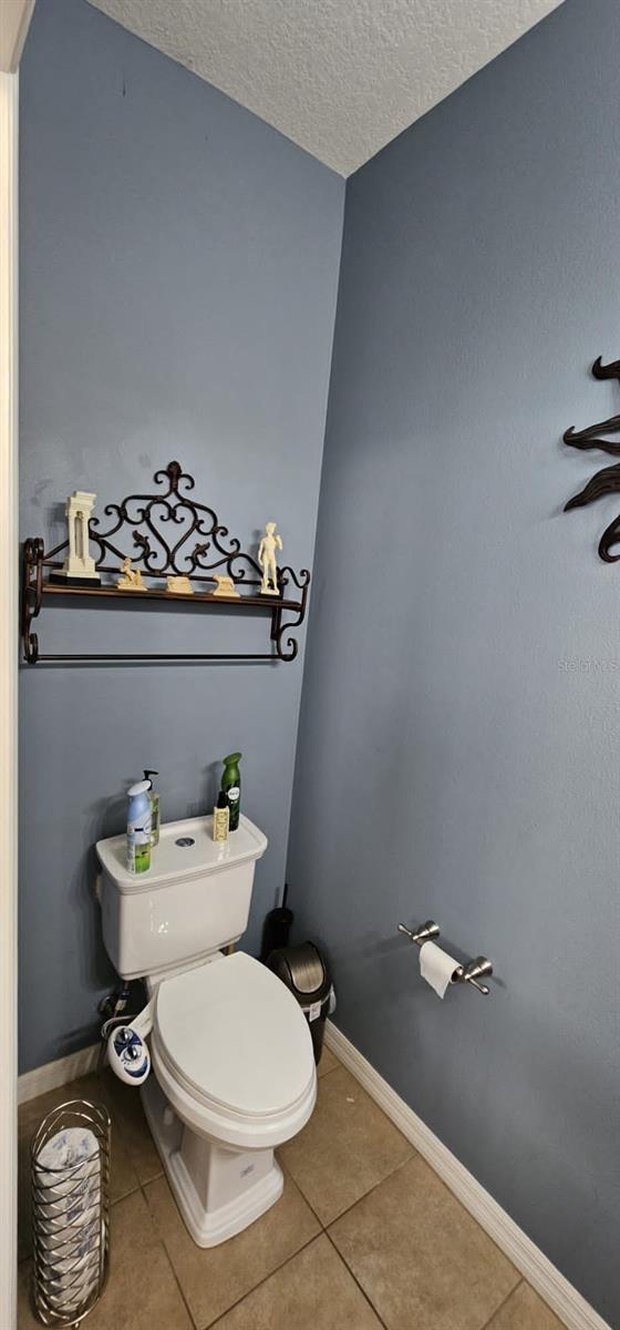 bathroom with a textured ceiling, toilet, and tile floors