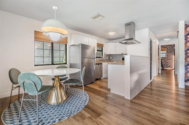 kitchen featuring decorative backsplash, extractor fan, light hardwood / wood-style flooring, white cabinetry, and appliances with stainless steel finishes