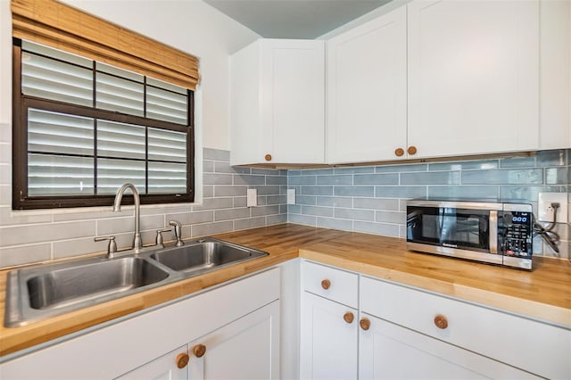 kitchen with butcher block countertops, decorative backsplash, sink, and white cabinets