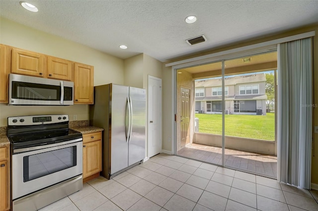 kitchen featuring a healthy amount of sunlight, stainless steel appliances, light tile floors, and dark stone countertops