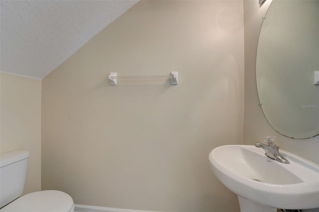 bathroom with lofted ceiling, toilet, a textured ceiling, and sink