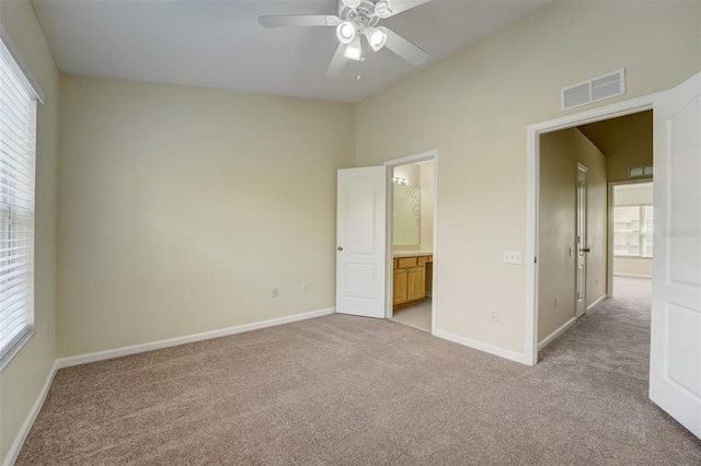 unfurnished bedroom featuring light colored carpet, connected bathroom, and multiple windows