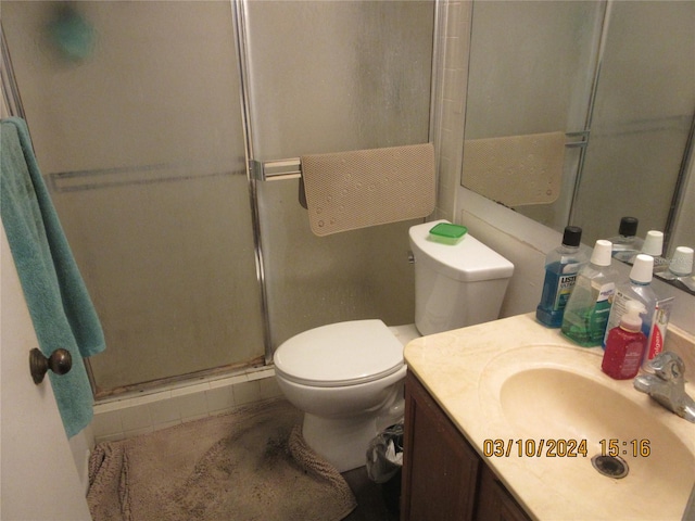 bathroom featuring a shower with door, toilet, and vanity