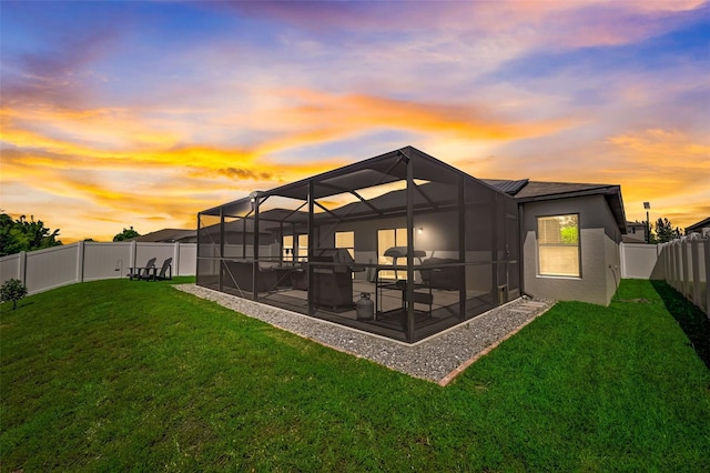 back house at dusk featuring a lanai, a patio area, and a yard