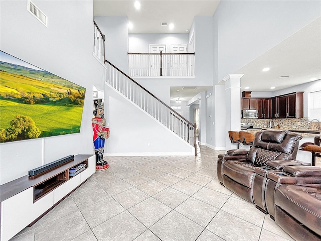 tiled living room with decorative columns, ceiling fan, and a towering ceiling