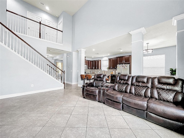 living room with light tile flooring, ceiling fan with notable chandelier, a towering ceiling, and ornate columns