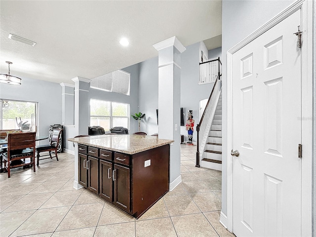 kitchen featuring kitchen peninsula, light stone counters, decorative columns, light tile flooring, and dark brown cabinetry