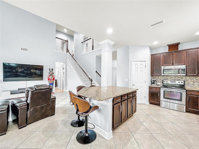 kitchen with backsplash, light tile flooring, a kitchen breakfast bar, stainless steel appliances, and ornate columns