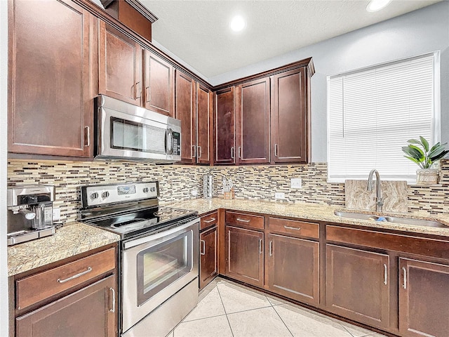 kitchen with stainless steel appliances, light tile floors, light stone countertops, backsplash, and sink