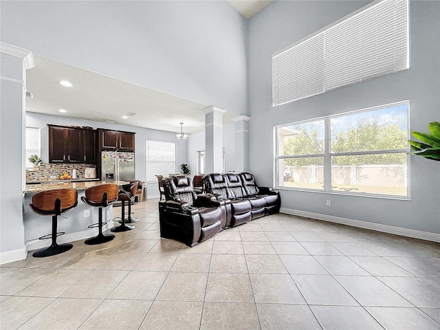 tiled living room featuring plenty of natural light, decorative columns, and a towering ceiling