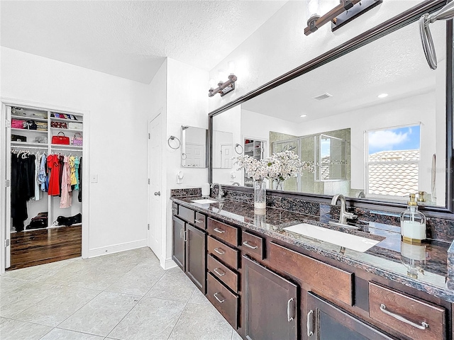 bathroom featuring a shower with shower door, a textured ceiling, dual bowl vanity, and tile flooring