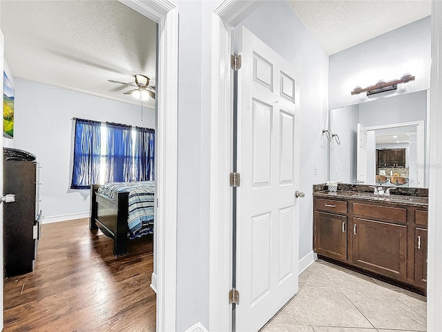 bathroom with a textured ceiling, large vanity, ceiling fan, and wood-type flooring