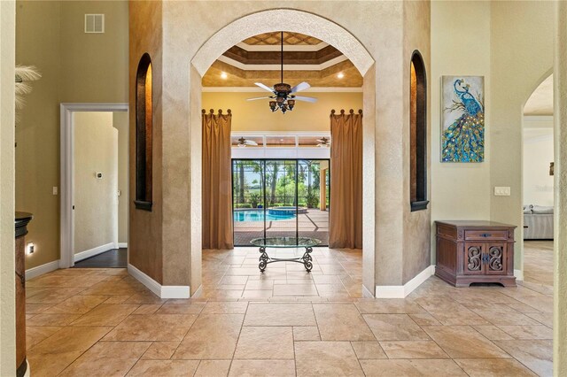 hall with a tray ceiling, ornamental molding, and a high ceiling