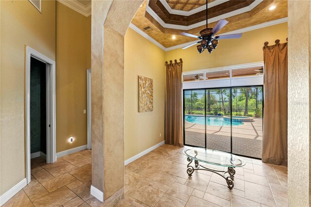 entrance foyer featuring a high ceiling, ceiling fan, light tile floors, a raised ceiling, and ornamental molding