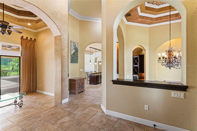 corridor with a raised ceiling, ornamental molding, a notable chandelier, and a towering ceiling