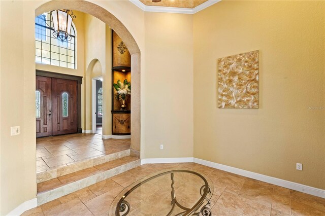 entryway featuring a notable chandelier, a towering ceiling, light tile flooring, and ornamental molding