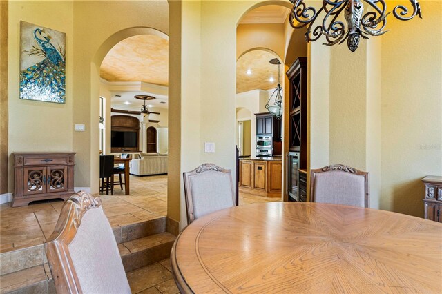 dining area with beverage cooler, ceiling fan with notable chandelier, light tile floors, and crown molding