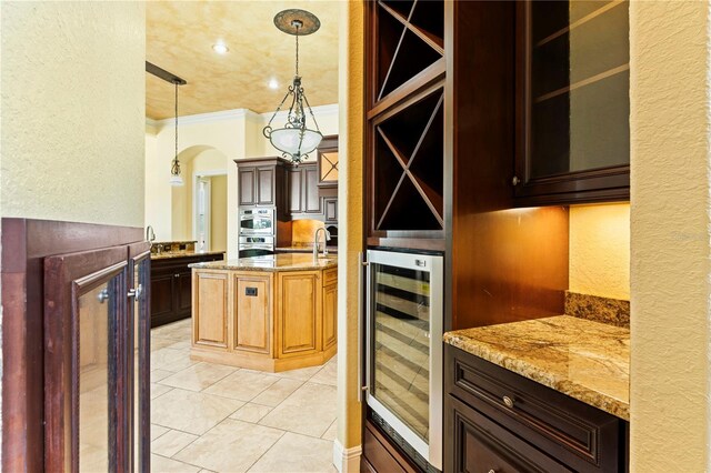 kitchen featuring beverage cooler, hanging light fixtures, light stone counters, and ornamental molding