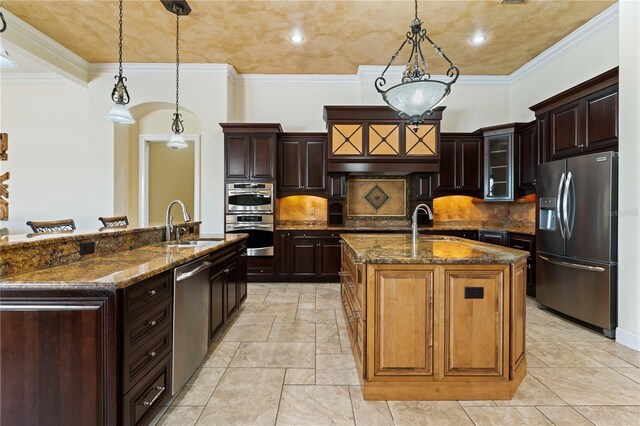 kitchen with pendant lighting, dark stone counters, appliances with stainless steel finishes, backsplash, and a kitchen island with sink