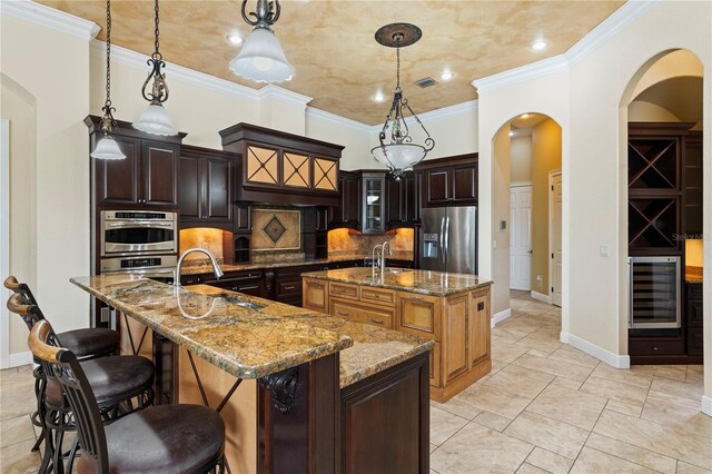 kitchen with hanging light fixtures, sink, stainless steel appliances, a center island with sink, and tasteful backsplash