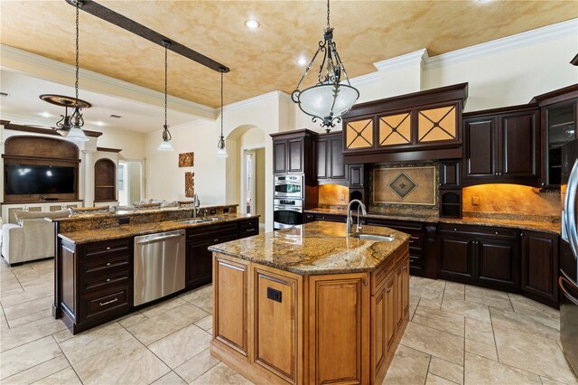 kitchen with an island with sink, pendant lighting, stainless steel appliances, dark stone countertops, and sink