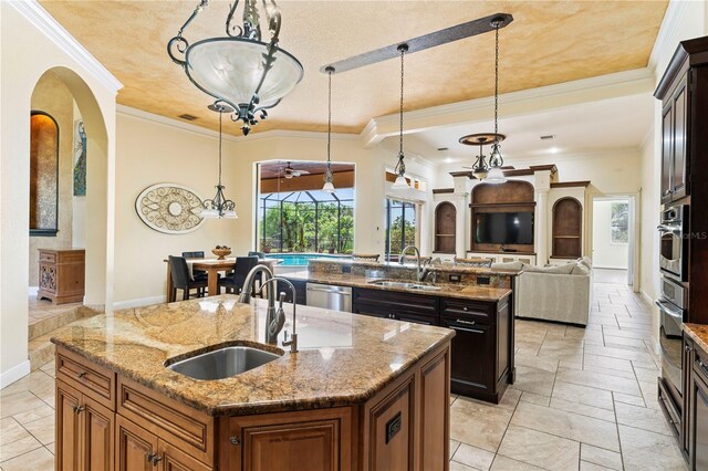 kitchen with a kitchen island with sink, appliances with stainless steel finishes, sink, pendant lighting, and ornamental molding