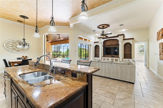 kitchen featuring ceiling fan with notable chandelier, sink, dark stone countertops, a center island with sink, and pendant lighting