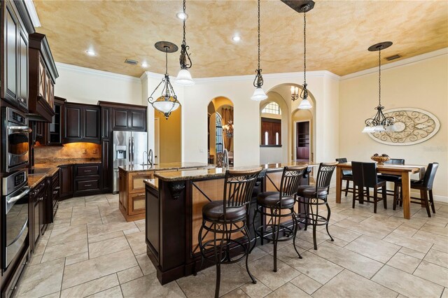 kitchen with appliances with stainless steel finishes, hanging light fixtures, backsplash, and a kitchen island with sink