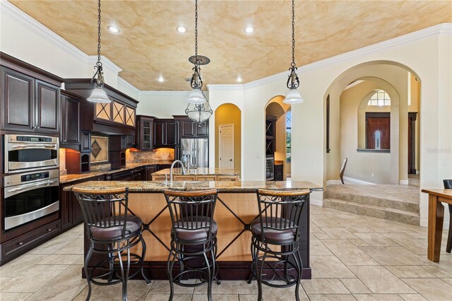 kitchen featuring a kitchen bar, hanging light fixtures, stainless steel appliances, and light tile flooring