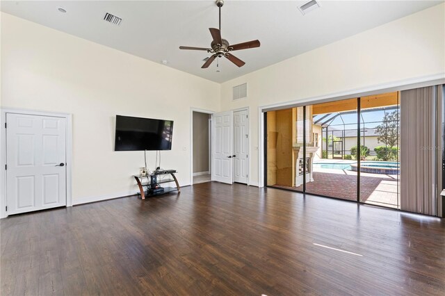 unfurnished living room featuring dark wood-type flooring, ceiling fan, and a towering ceiling