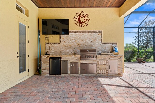 view of patio featuring glass enclosure, grilling area, and an outdoor kitchen