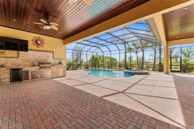 view of swimming pool with ceiling fan, an in ground hot tub, glass enclosure, a patio, and an outdoor kitchen