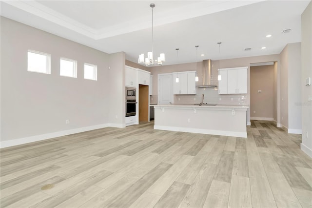 kitchen with a center island with sink, white cabinets, wall chimney range hood, and light hardwood / wood-style flooring