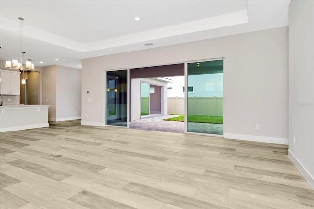 unfurnished living room with light wood-type flooring, a tray ceiling, and an inviting chandelier