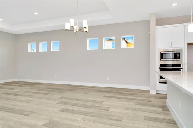 unfurnished dining area featuring light wood-type flooring, a raised ceiling, and a wealth of natural light