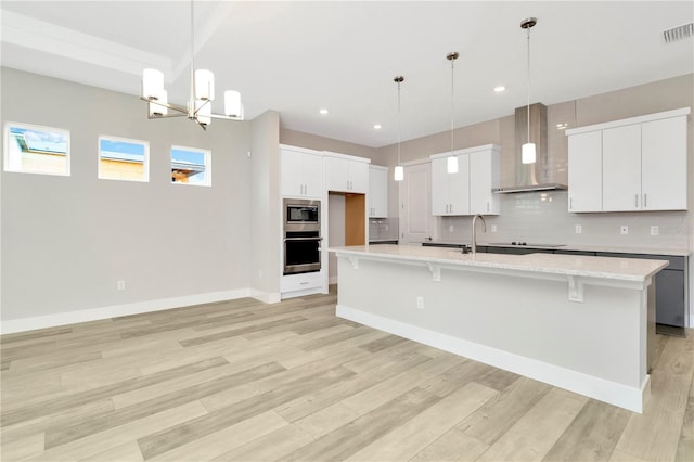 kitchen with white cabinetry, hanging light fixtures, stainless steel appliances, wall chimney range hood, and light hardwood / wood-style floors