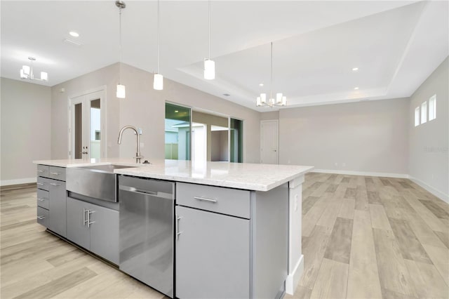 kitchen featuring gray cabinetry, hanging light fixtures, stainless steel dishwasher, an island with sink, and light hardwood / wood-style floors