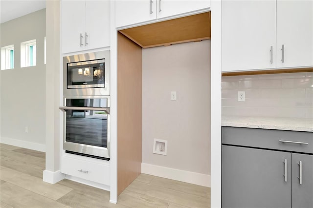 kitchen featuring stainless steel microwave, backsplash, light hardwood / wood-style floors, light stone counters, and white cabinetry