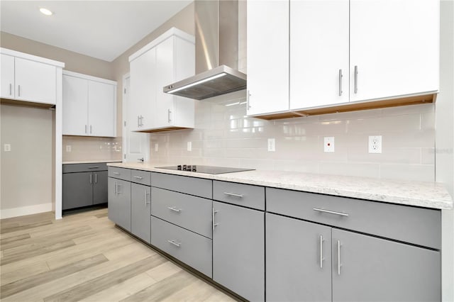 kitchen with light hardwood / wood-style floors, wall chimney exhaust hood, black electric cooktop, gray cabinets, and white cabinetry